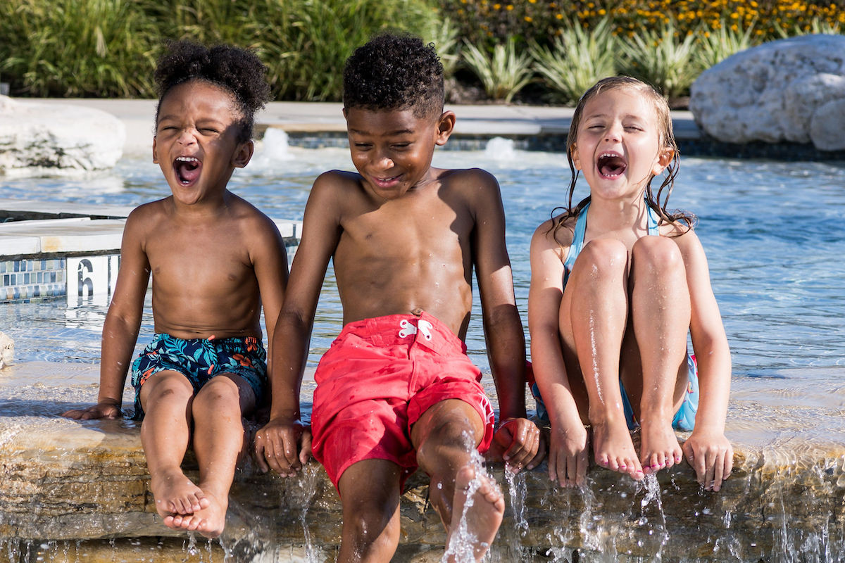3 kids sitting on the edge of a pool splashing water
